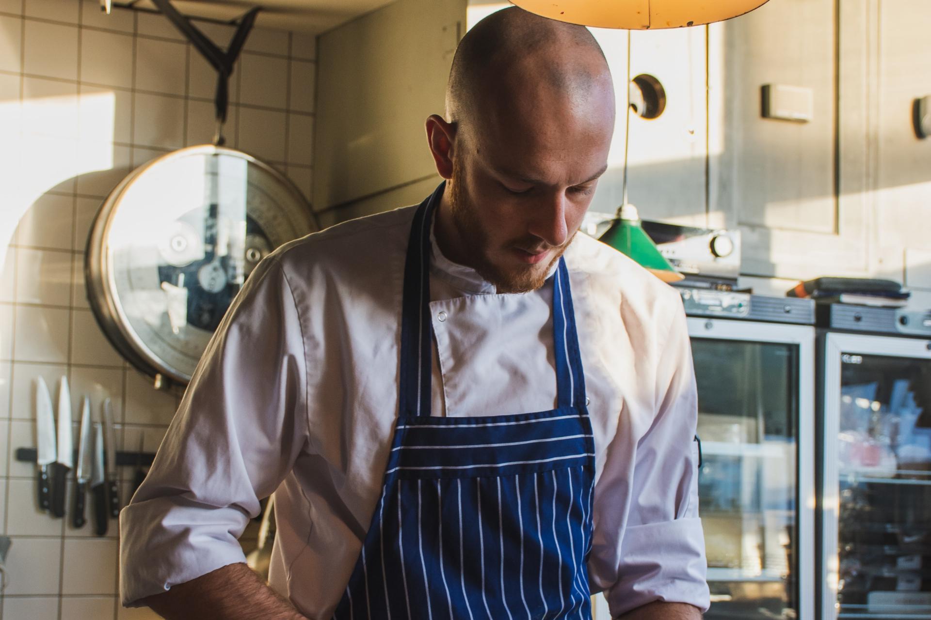 Chef calvo che guarda in basso mentre lavora in una cucina