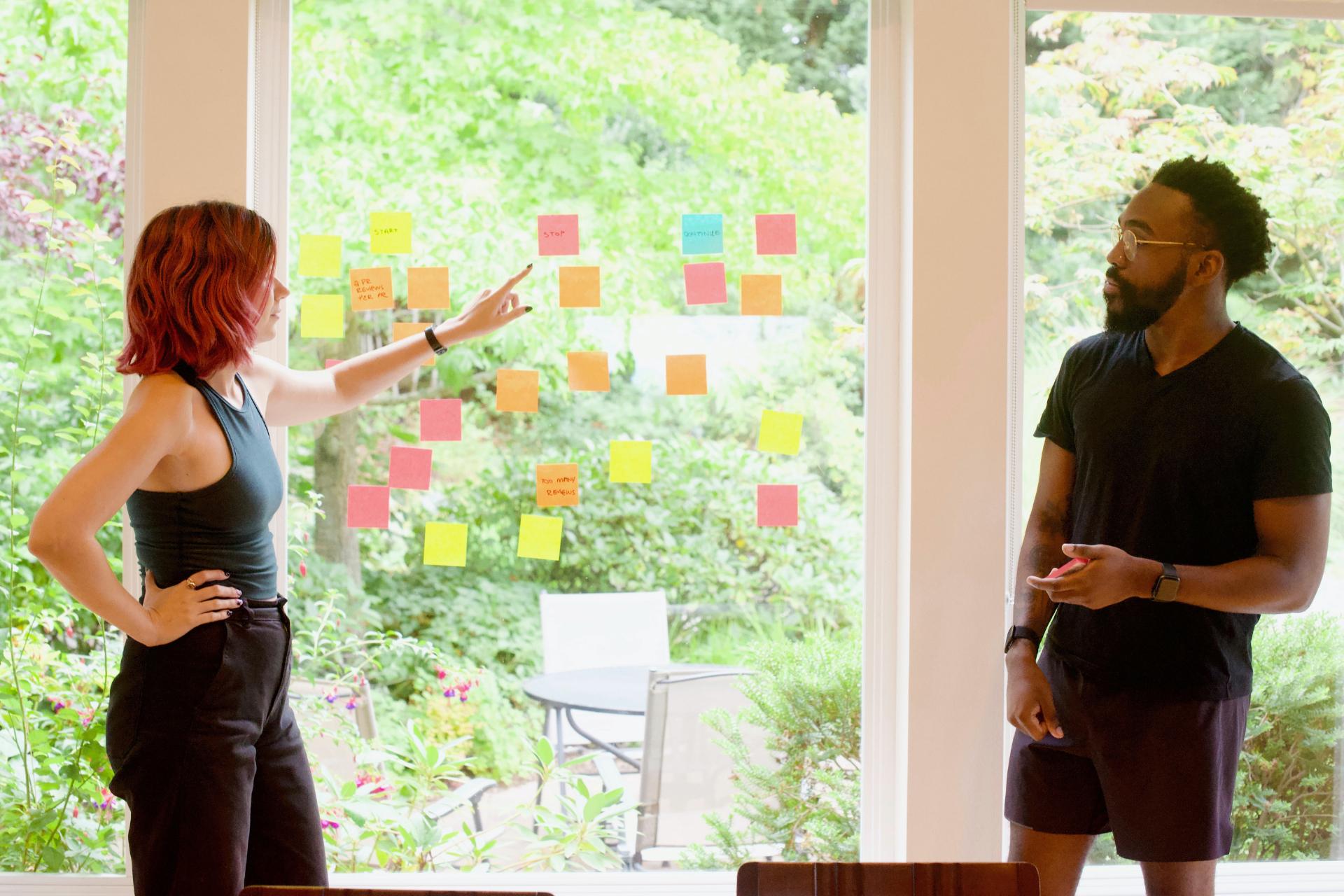 Donna e uomo che fanno il brainstorming di idee per lo slogan con post-it su vetro