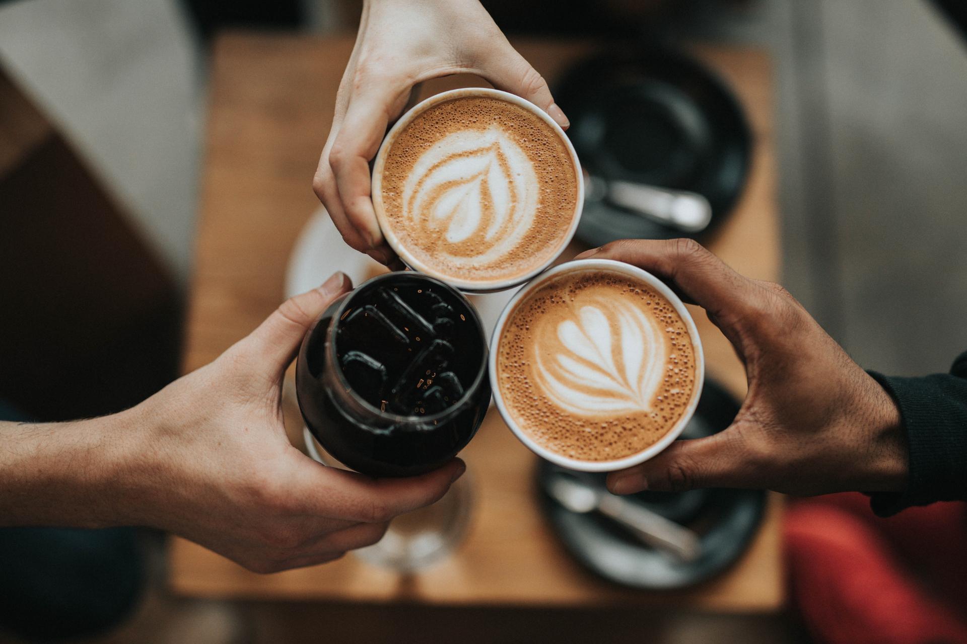 Drei Personen stoßen mit Kaffeegetränken an