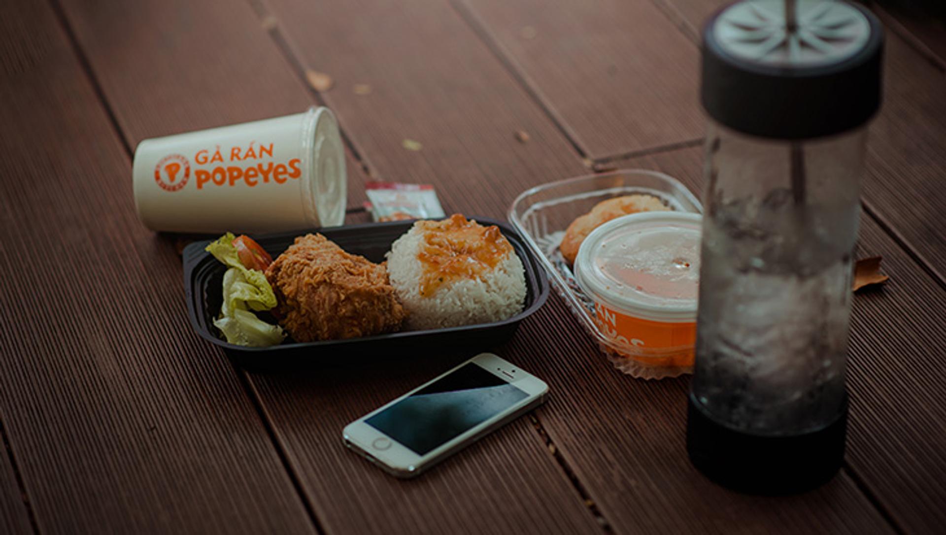 Comida para llevar de la cadena de restaurantes Popeyes en una mesa y cerca de un smartphone