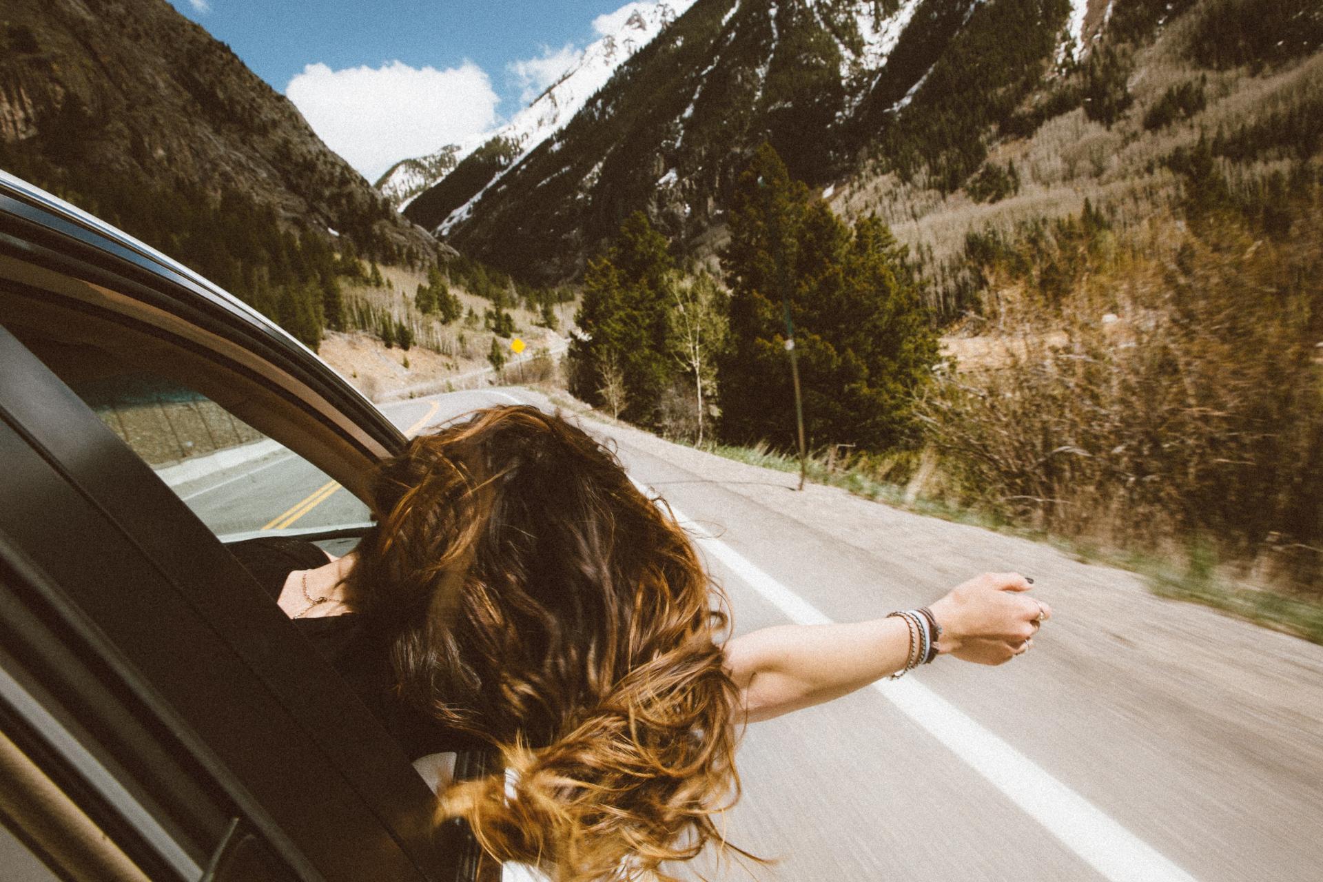 girl in passenger's seat putting her head out the window to feel the wind