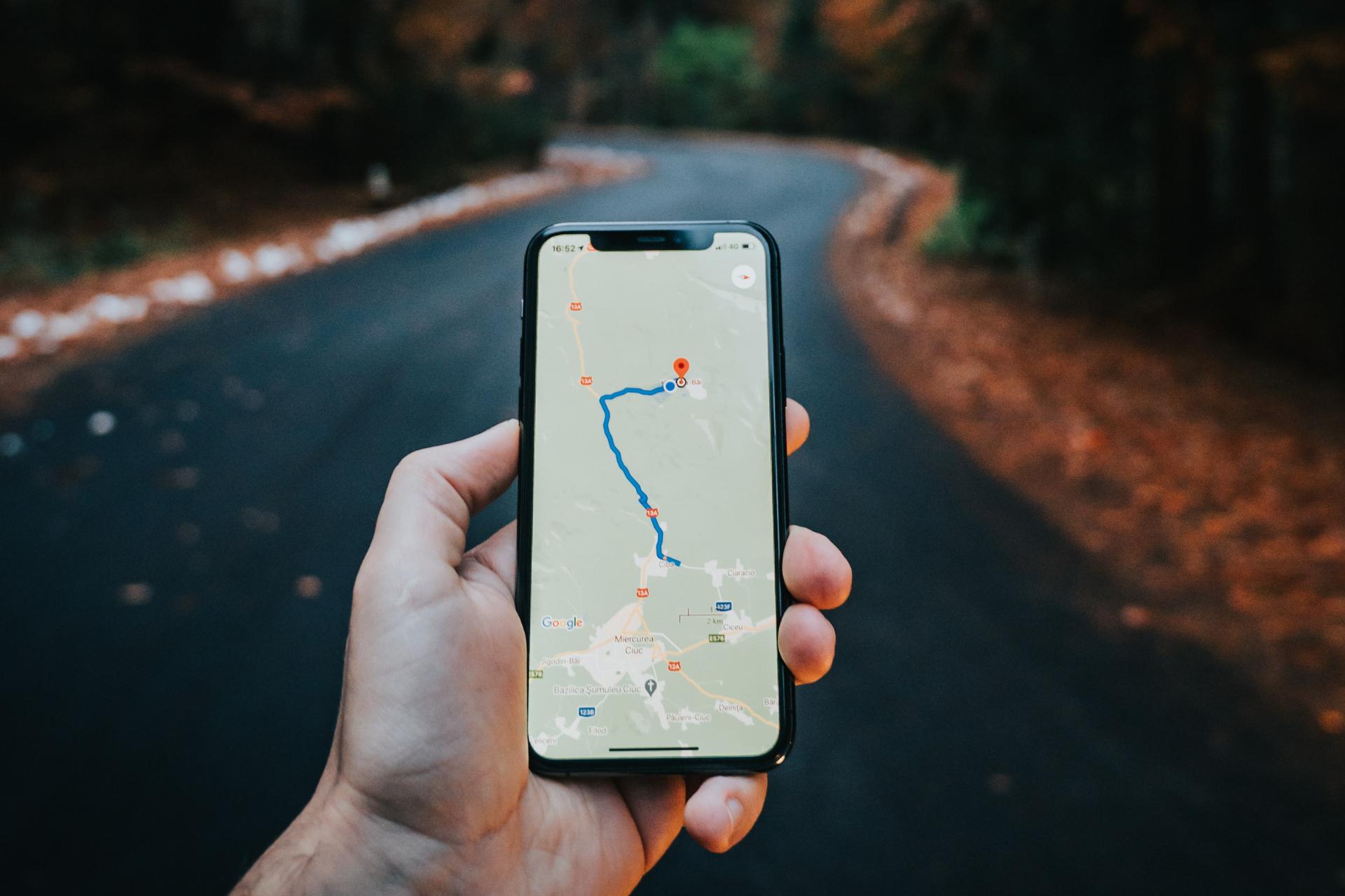 Persona parada en medio de la carretera mientras sostiene un teléfono que muestra mapas de Google con una ubicación señalada