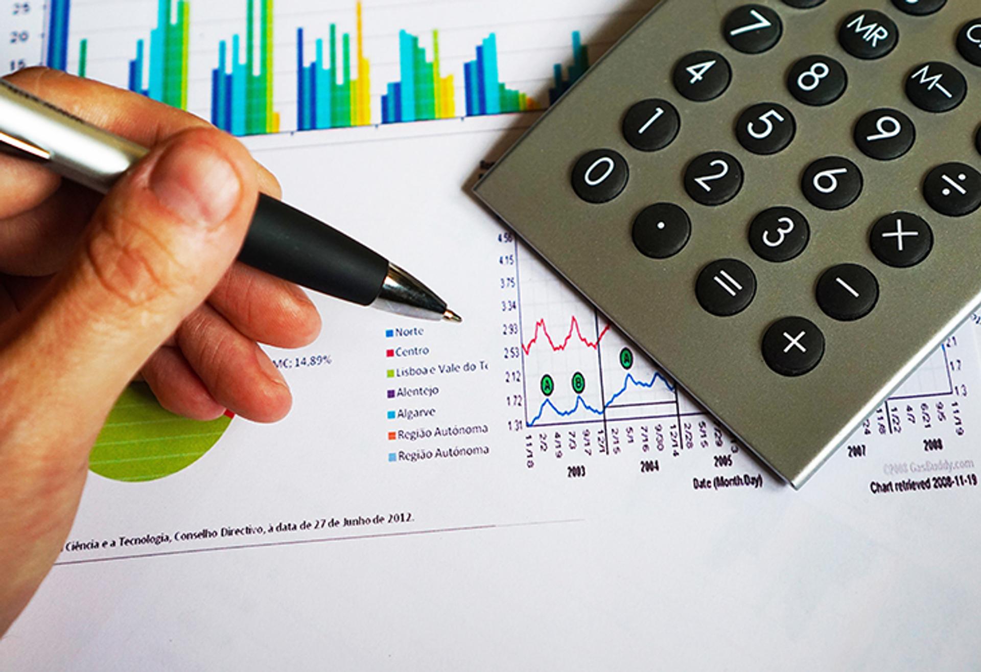 hand holding pen over charts and calculator