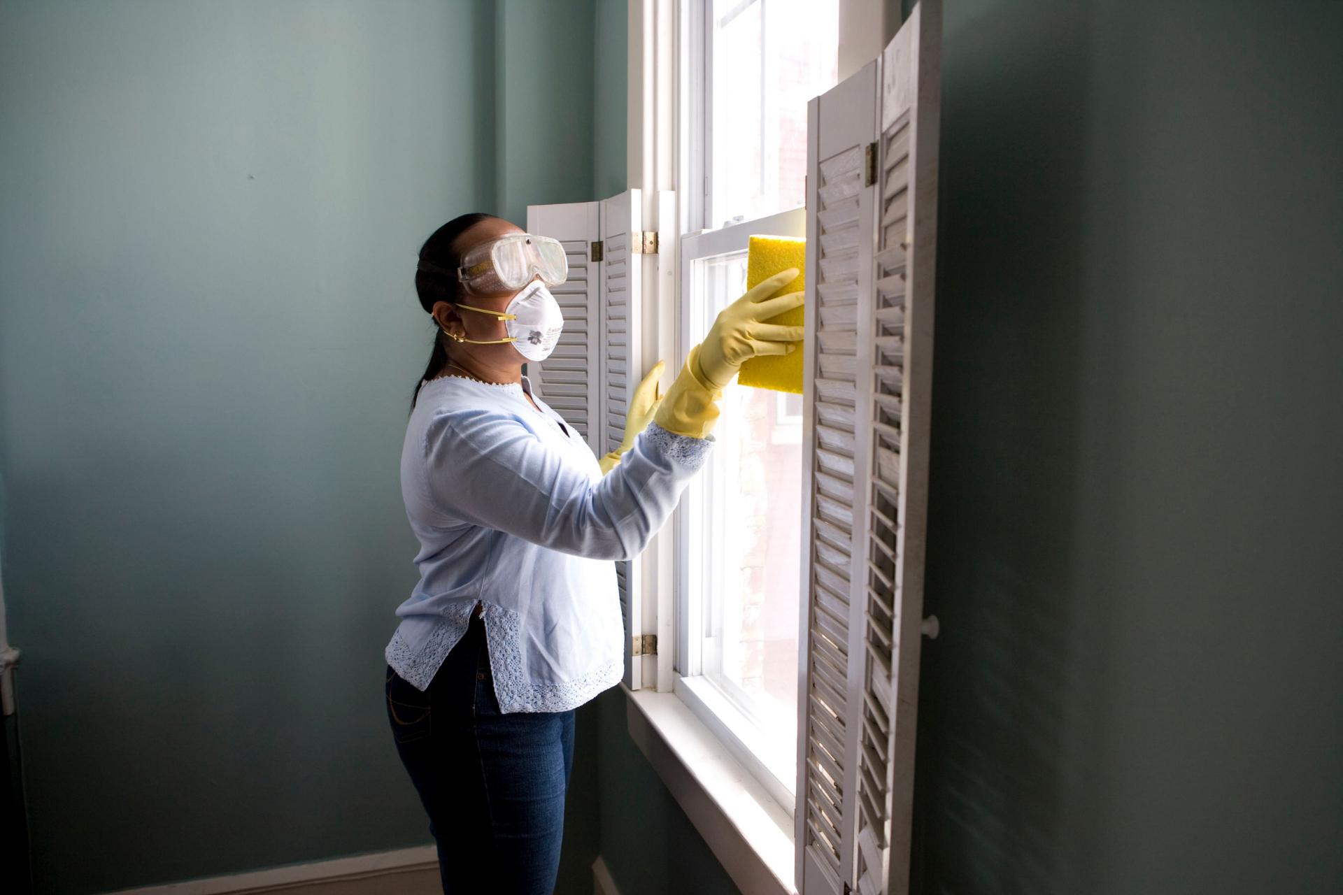 Señora limpiando ventana mientras usa equipo de protección
