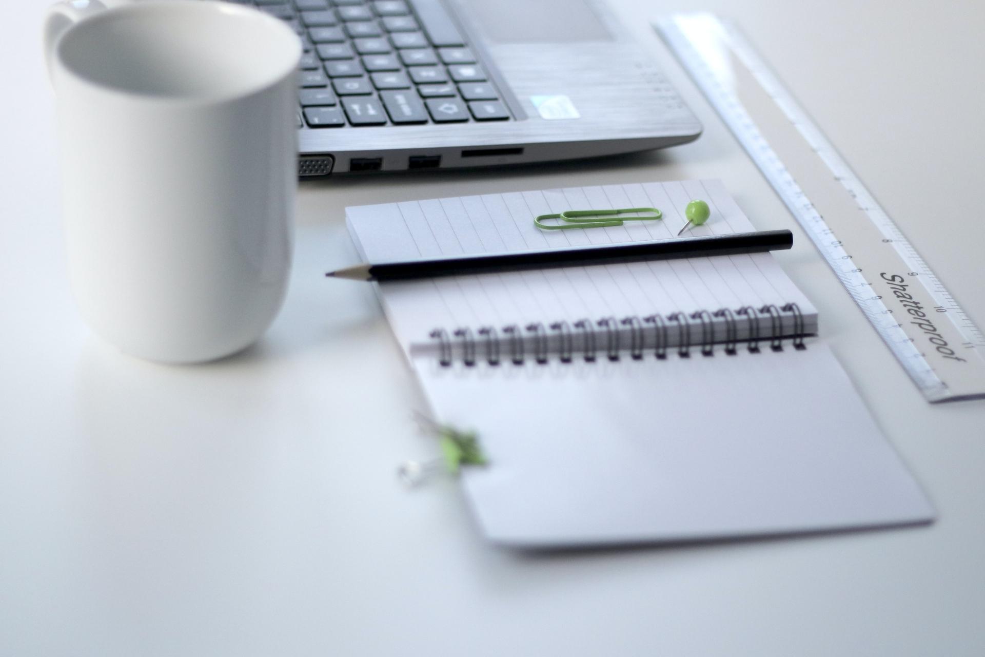 Laptop, Lineal, Becher und Notizblock auf dem Schreibtisch