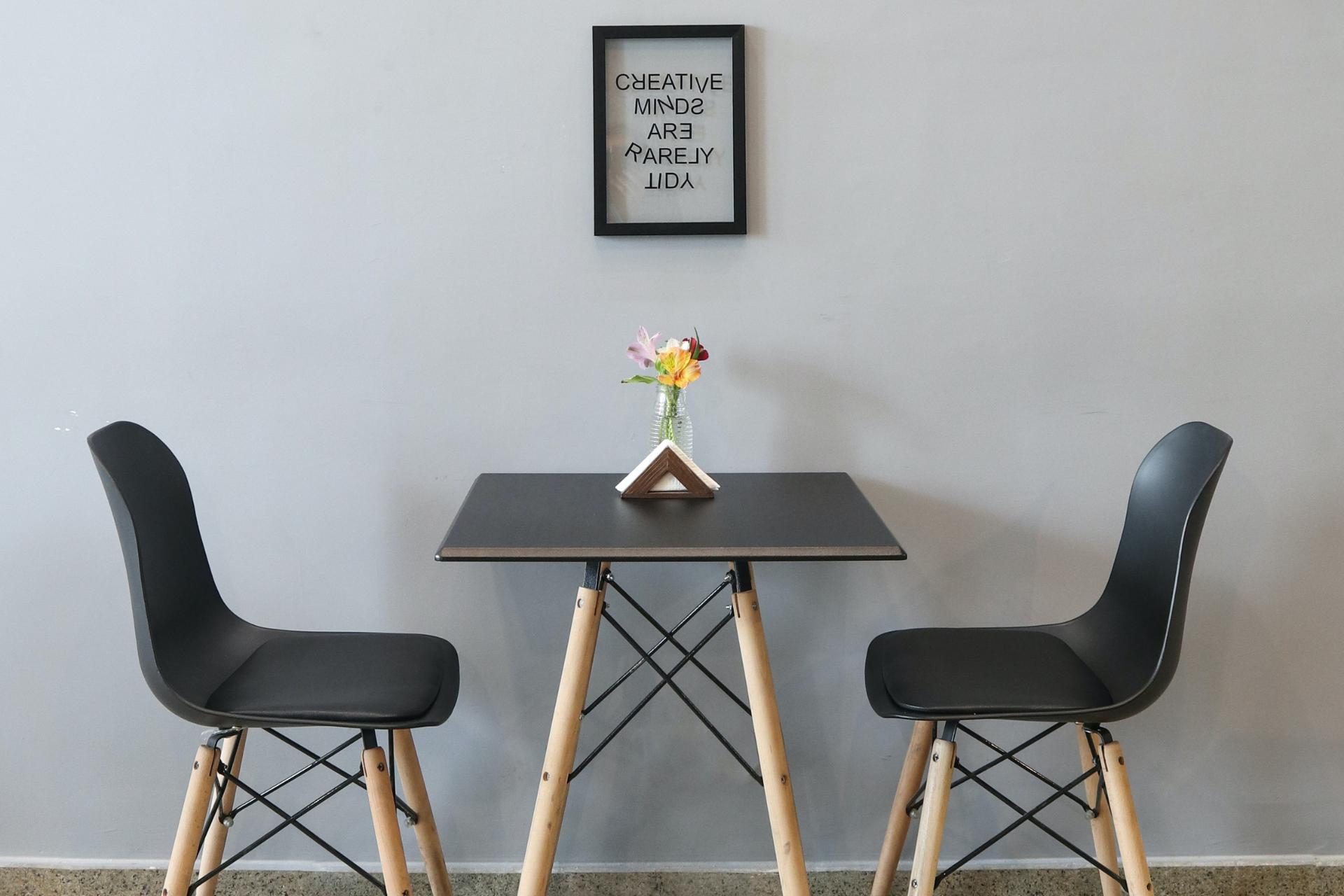 sillas y mesa pequeña de restaurante con sostenedor de servilletas, flores, y un cuadro en la pared