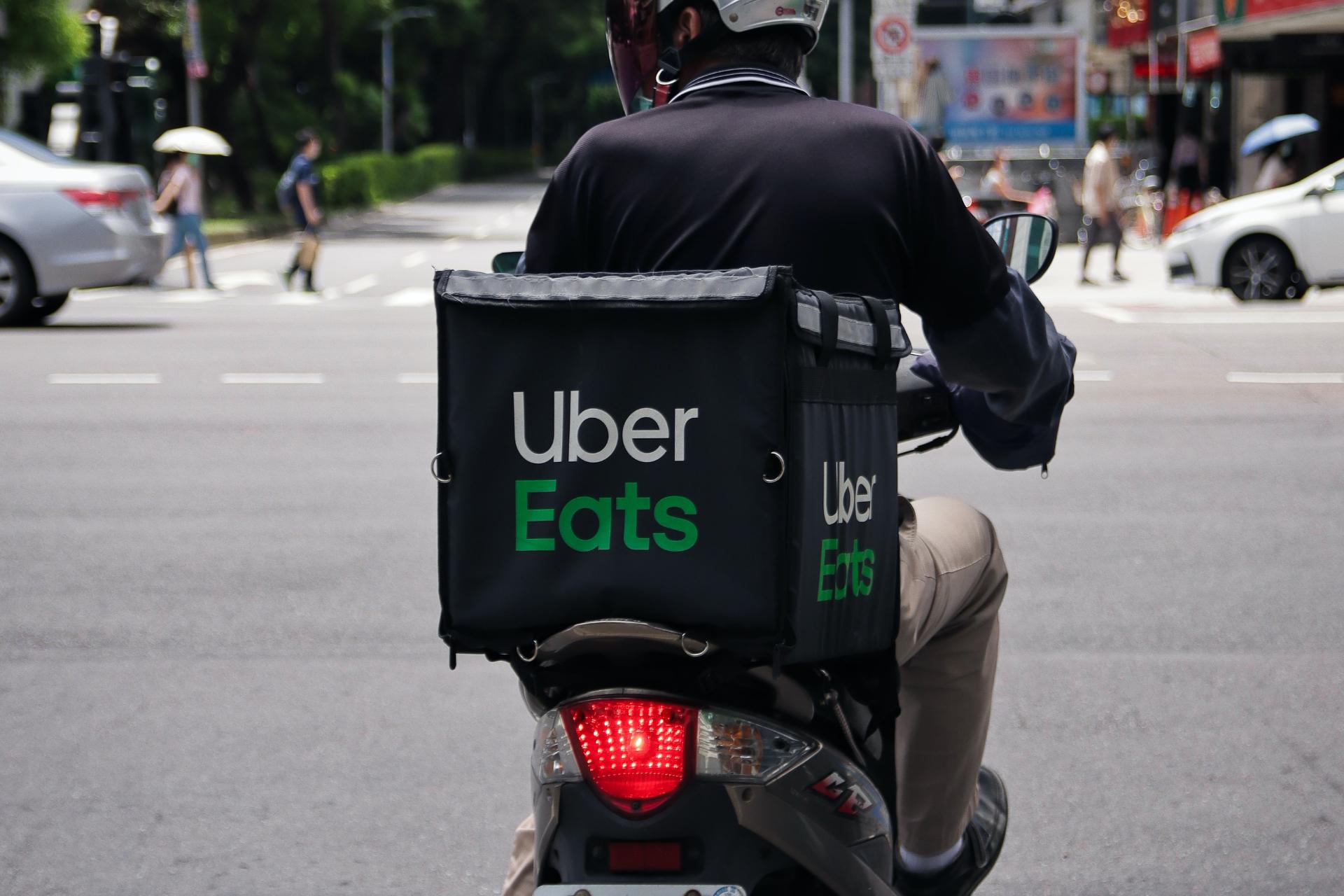 Bezorger van uber eet rijdende vespa