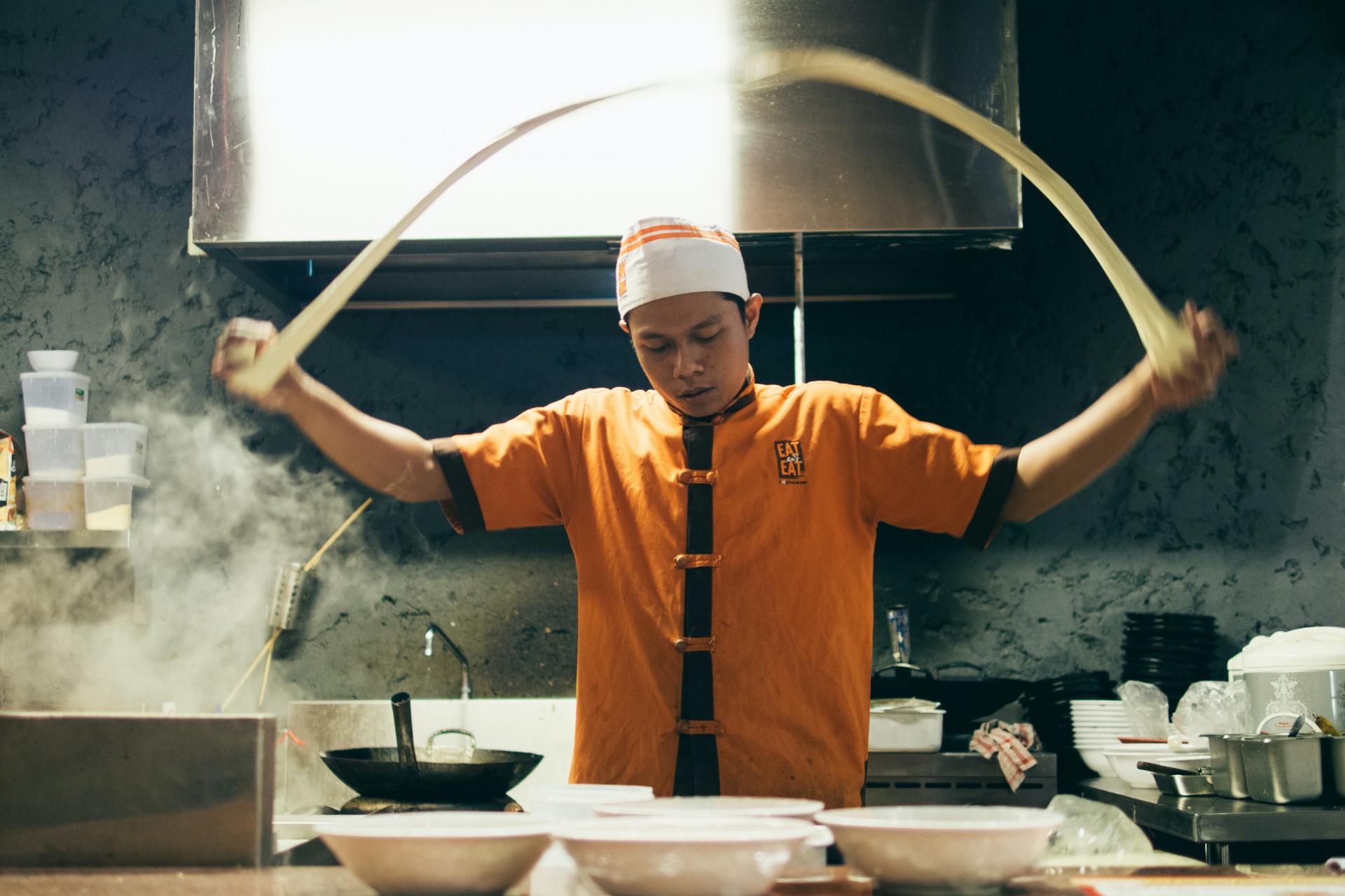 hombre estirando masa de algun tipo en una amplia zona de producción de cocina de restaurante