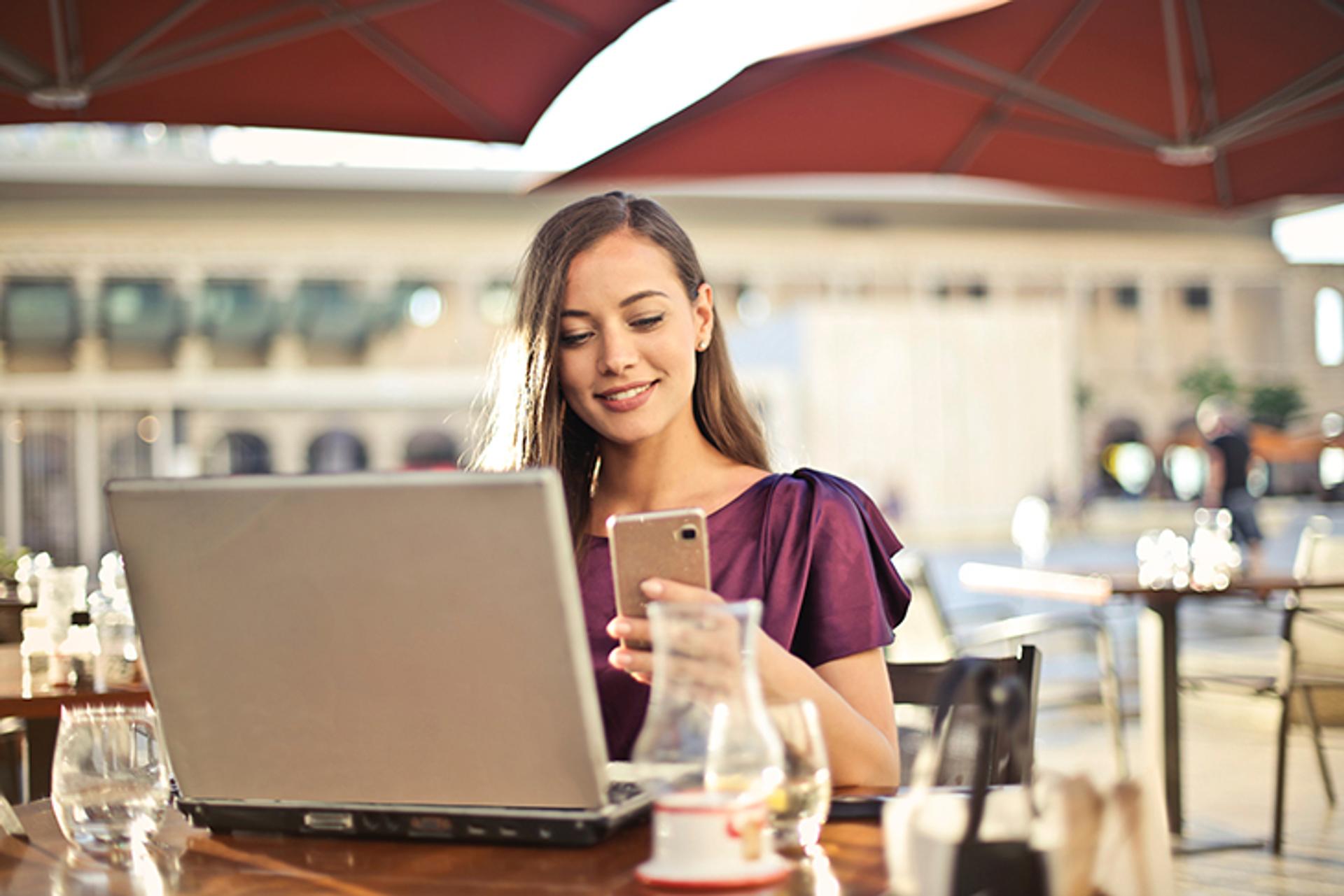 mujer en café usando una computadora portátil y un teléfono inteligente