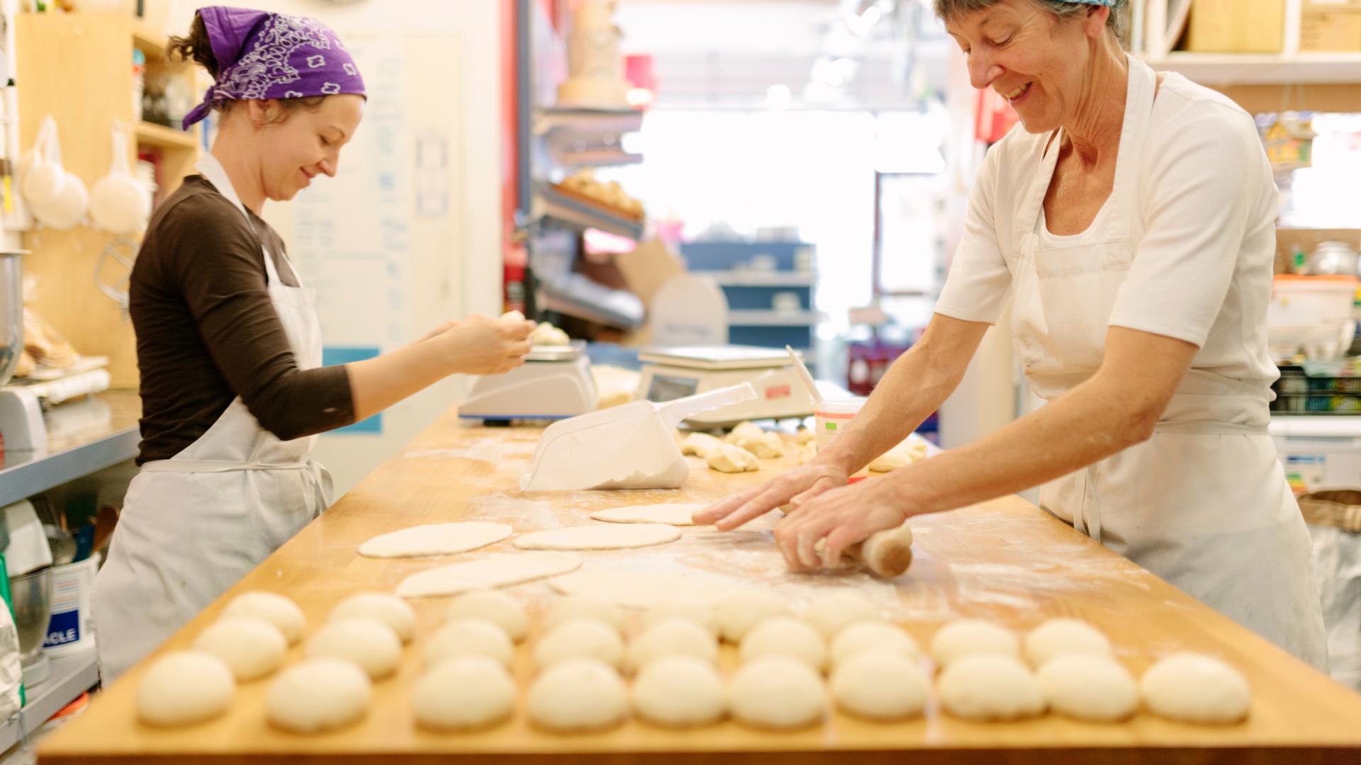 Damen, die an Teig arbeiten und an den Tischen einer Bäckerei lächeln