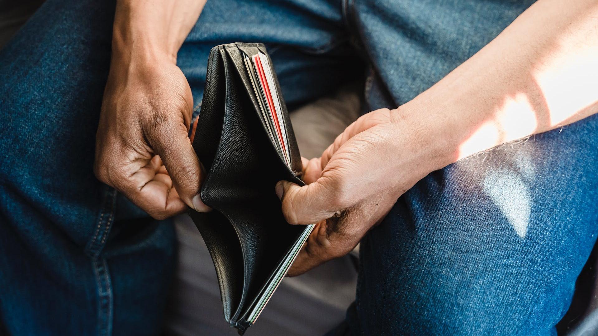 Mann öffnet leere Brieftasche, um darzustellen, dass er pleite ist