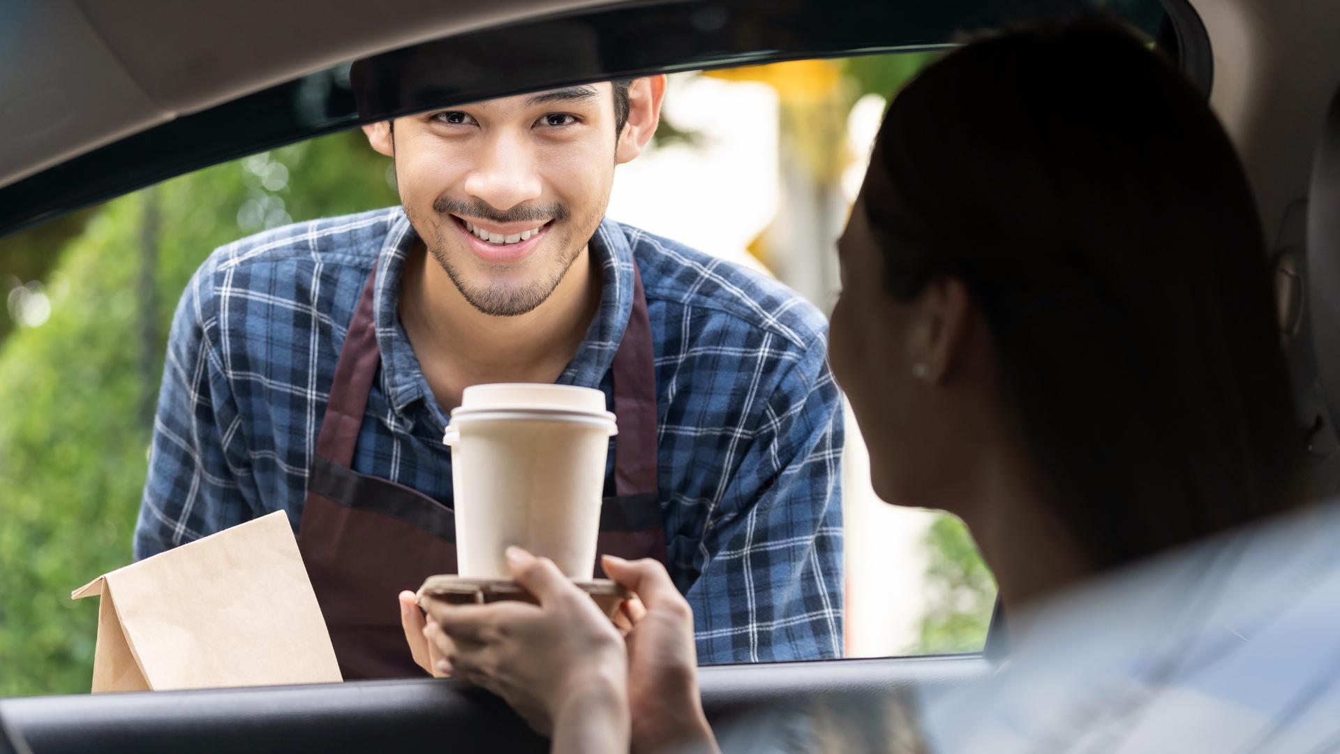 Mitarbeiter liefert Essen am Autofenster des Kunden aus