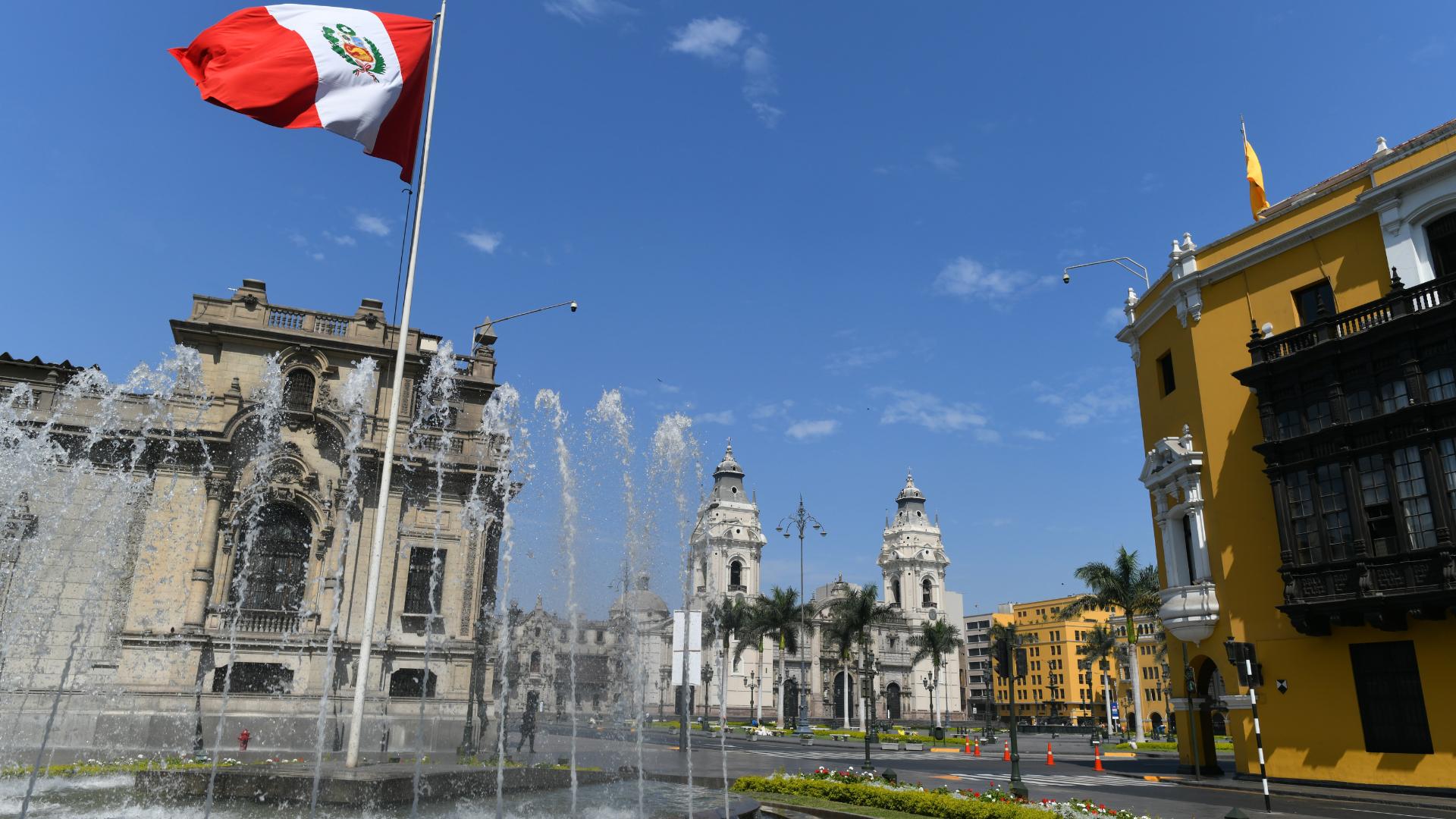 Plaza peruana con fuente y bandera rodeada de coloridos edificios