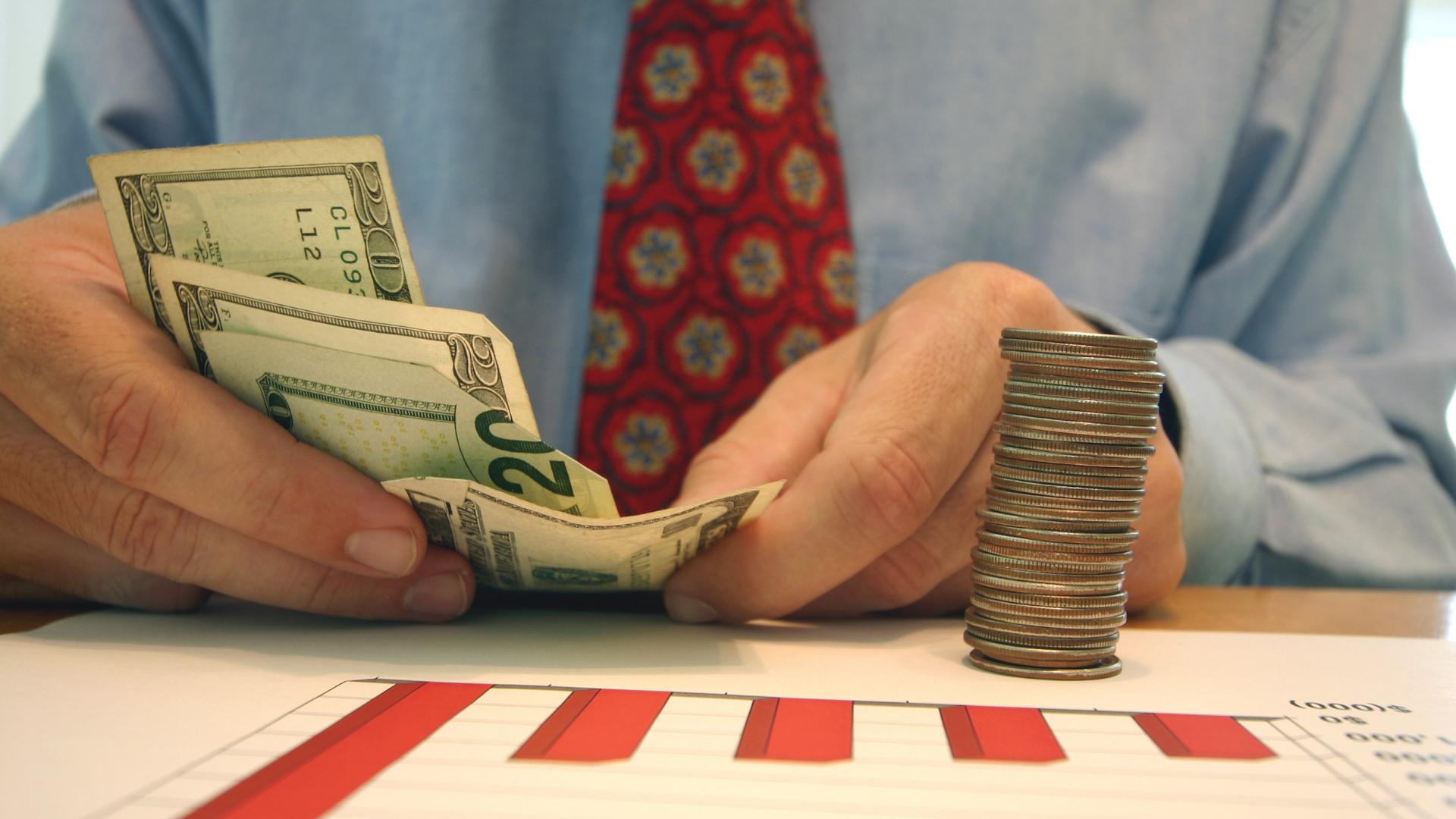 manager counting money on top of document with charts to symbolize profit margins