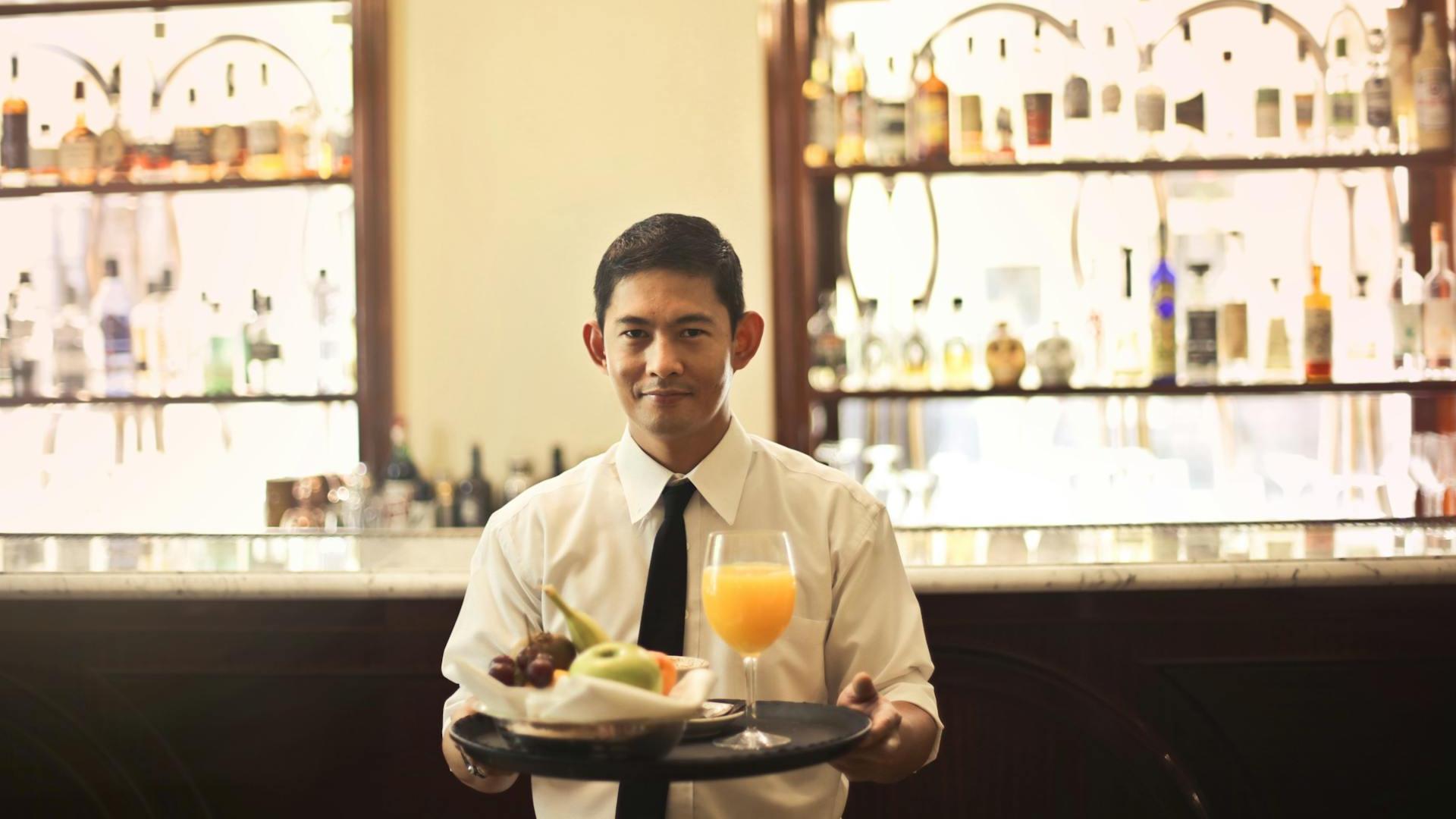 camarero de restaurante sonriendo mientras sostiene una bandeja con comida