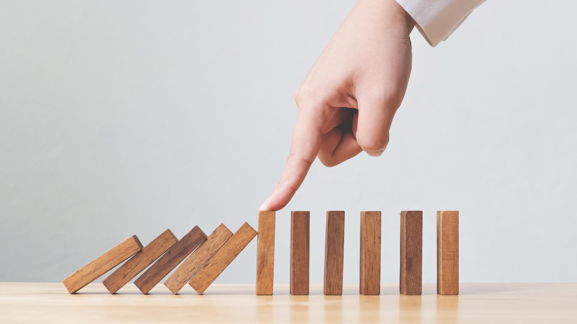 person holding wooden dominoes to represent risk management