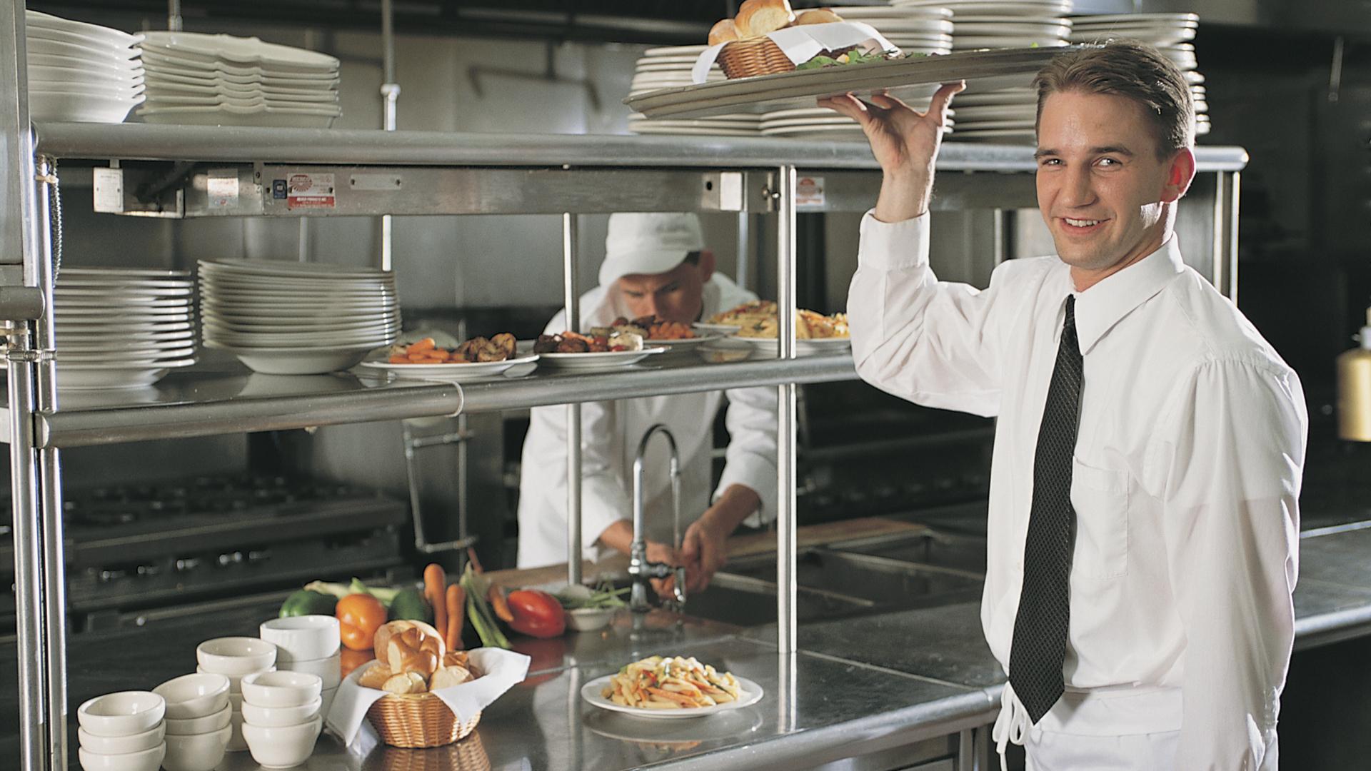 Kellner lächelt in der Küche, während er Geschirr trägt